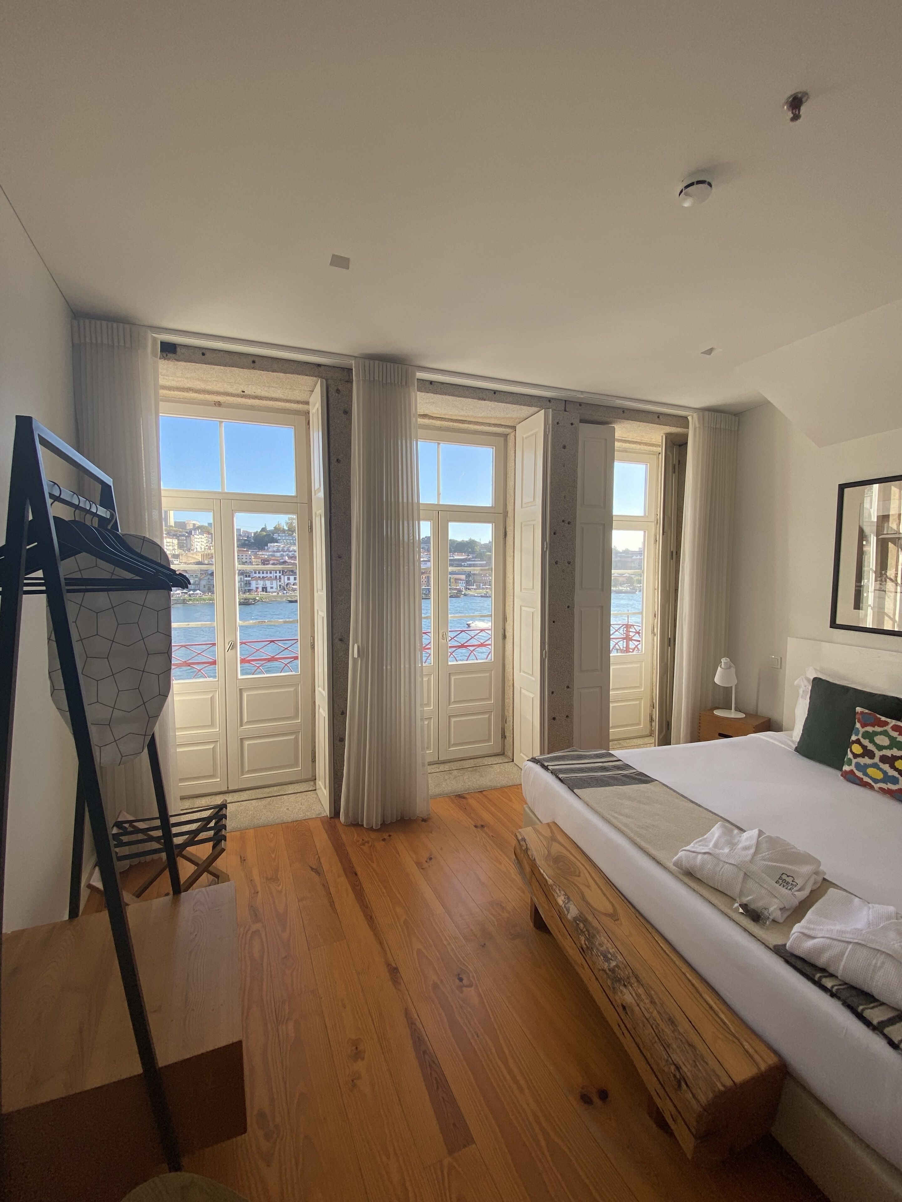 Een hotelkamer met een groot bed, houten vloeren, uitzicht op zee en een balkon.