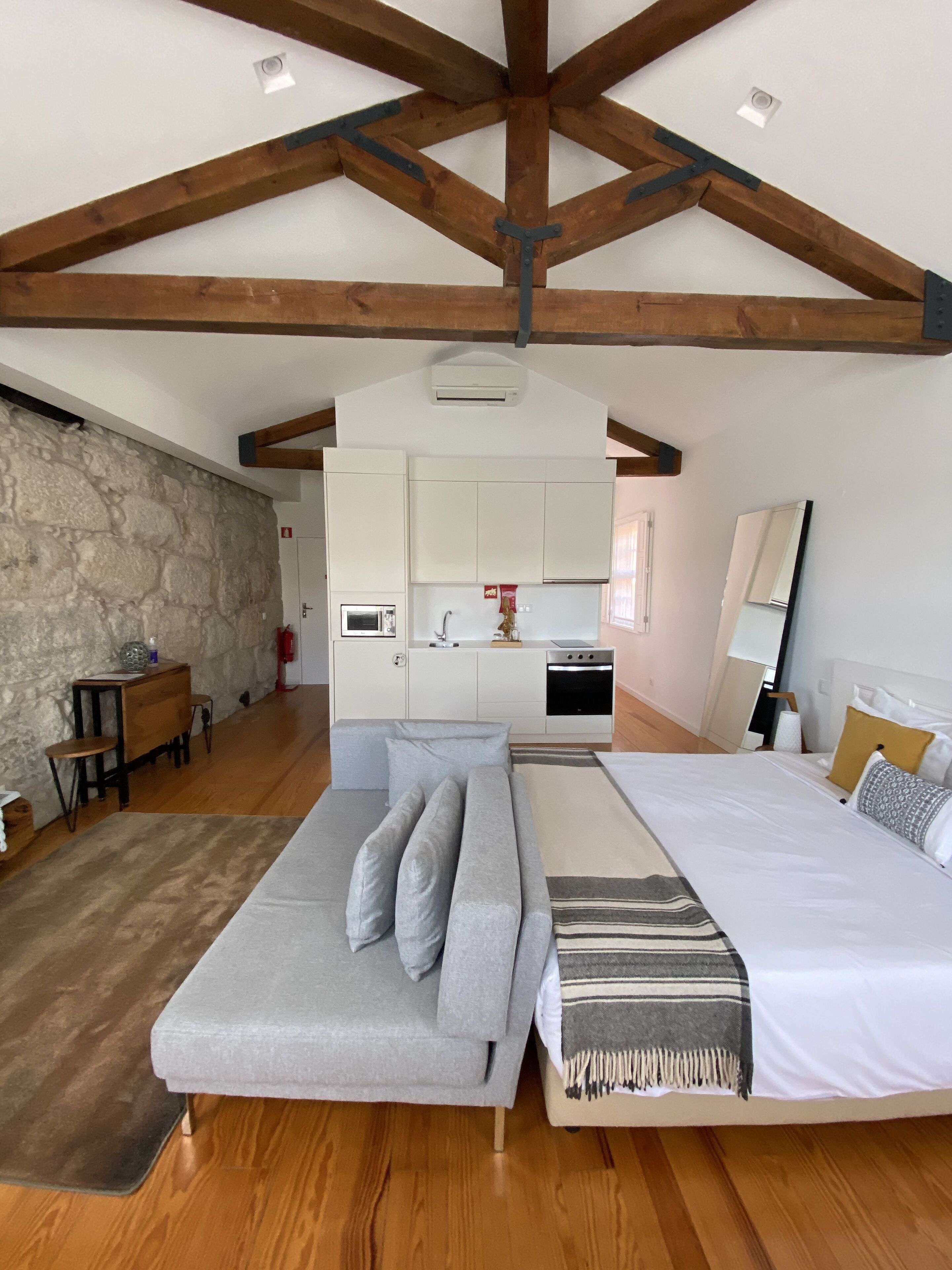A spacious bedroom with a large bed, a sofa, and a kitchen area in the background.