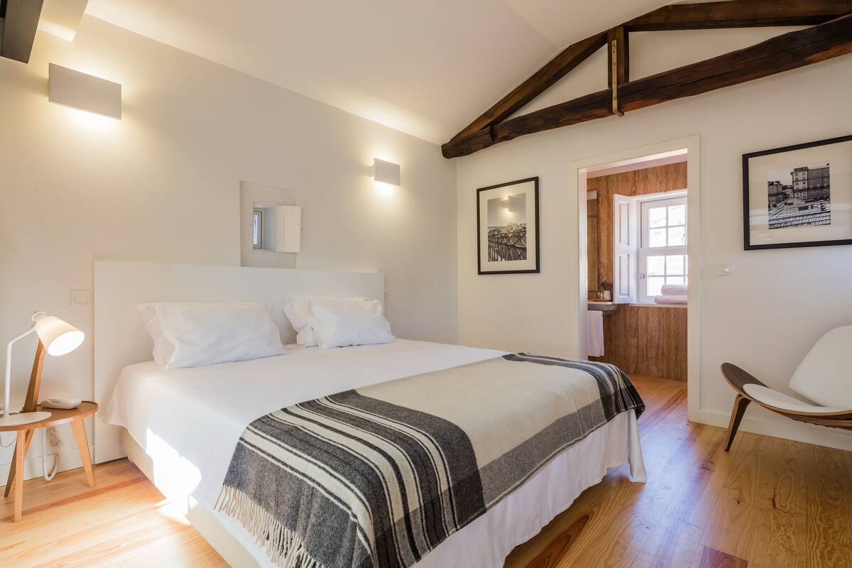 Une chambre avec un grand lit, des lampes de chevet, un plancher en bois, une chaise et une porte donnant sur une salle de bain.