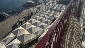 Un balcon donnant sur un port, agrémenté d’une rangée de parasols et d’une rambarde rouge.