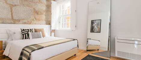 A bedroom with a stone wall, a bed with a striped blanket, a window, and a radiator.