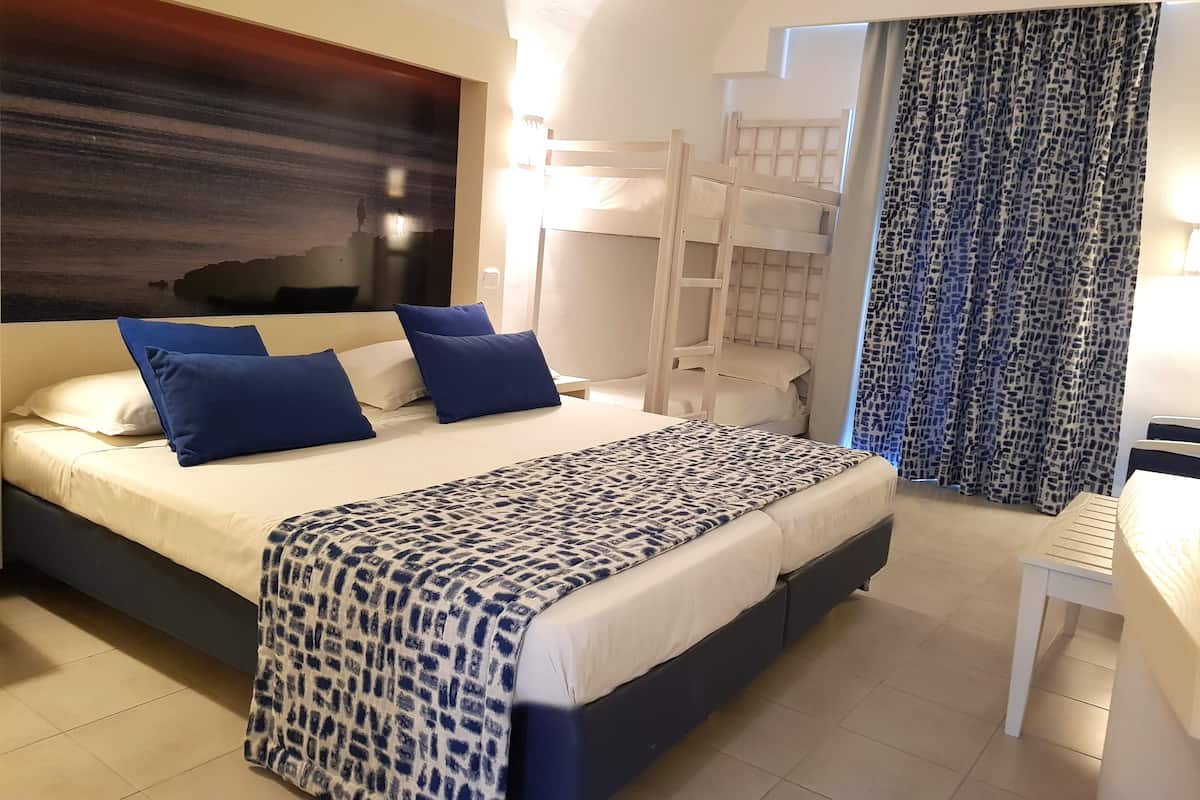A hotel room with a large bed, a bunk bed, a desk, and a patterned bedspread.