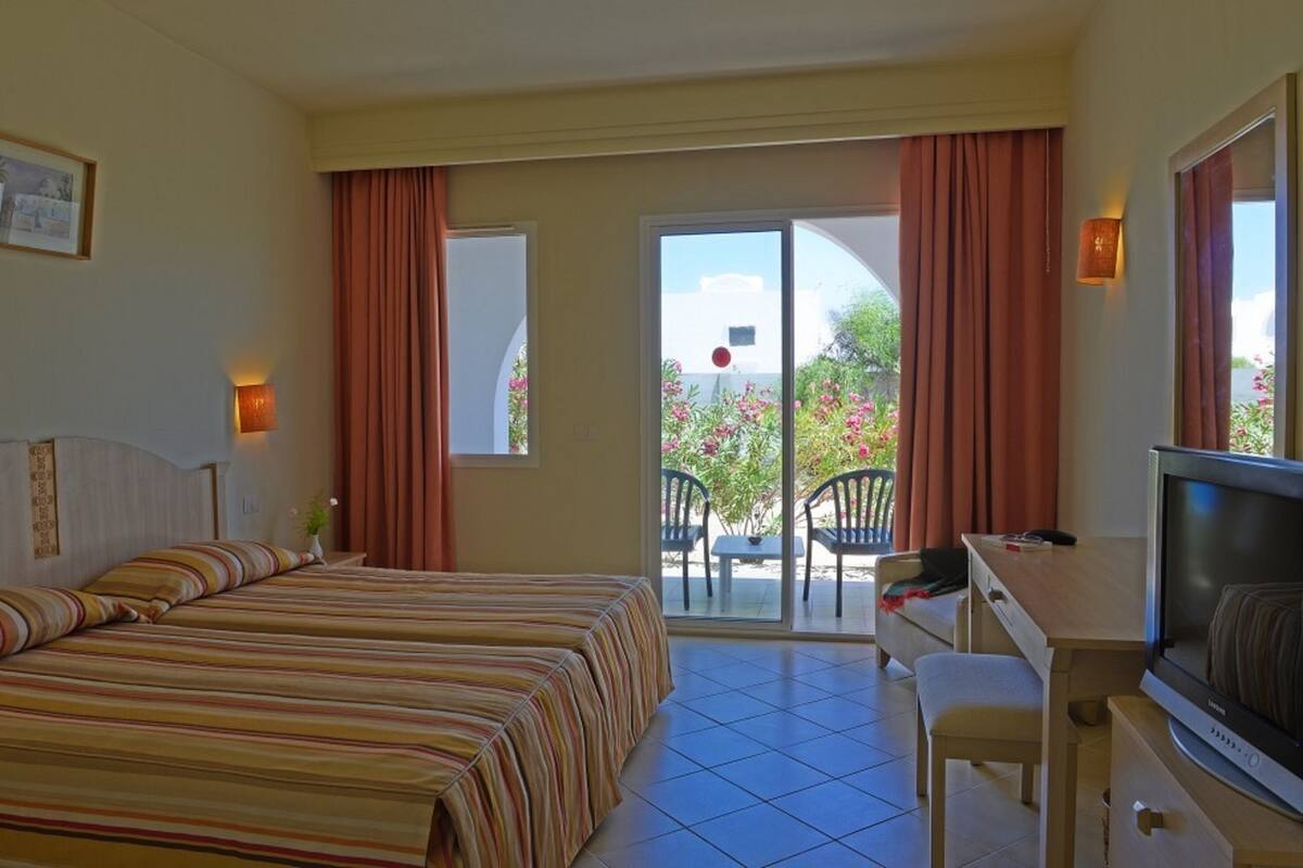A hotel room with a bed, a desk with a television, and a balcony with chairs and a table.