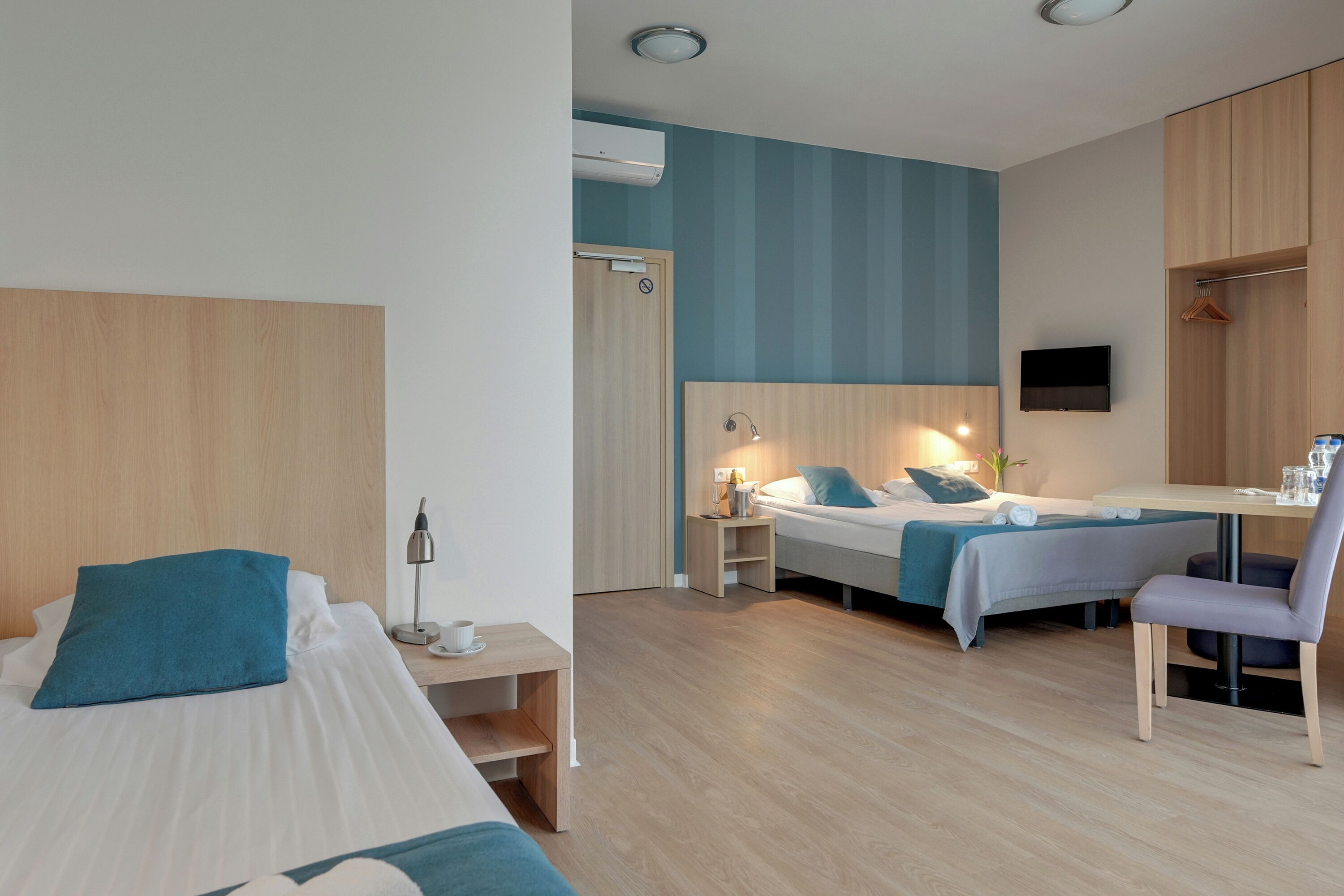 Ett hotellrum med två sängar, ett skrivbord, en stol, en TV och en garderob.