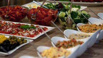 A buffet table with various dishes including salads, vegetables, and pasta.