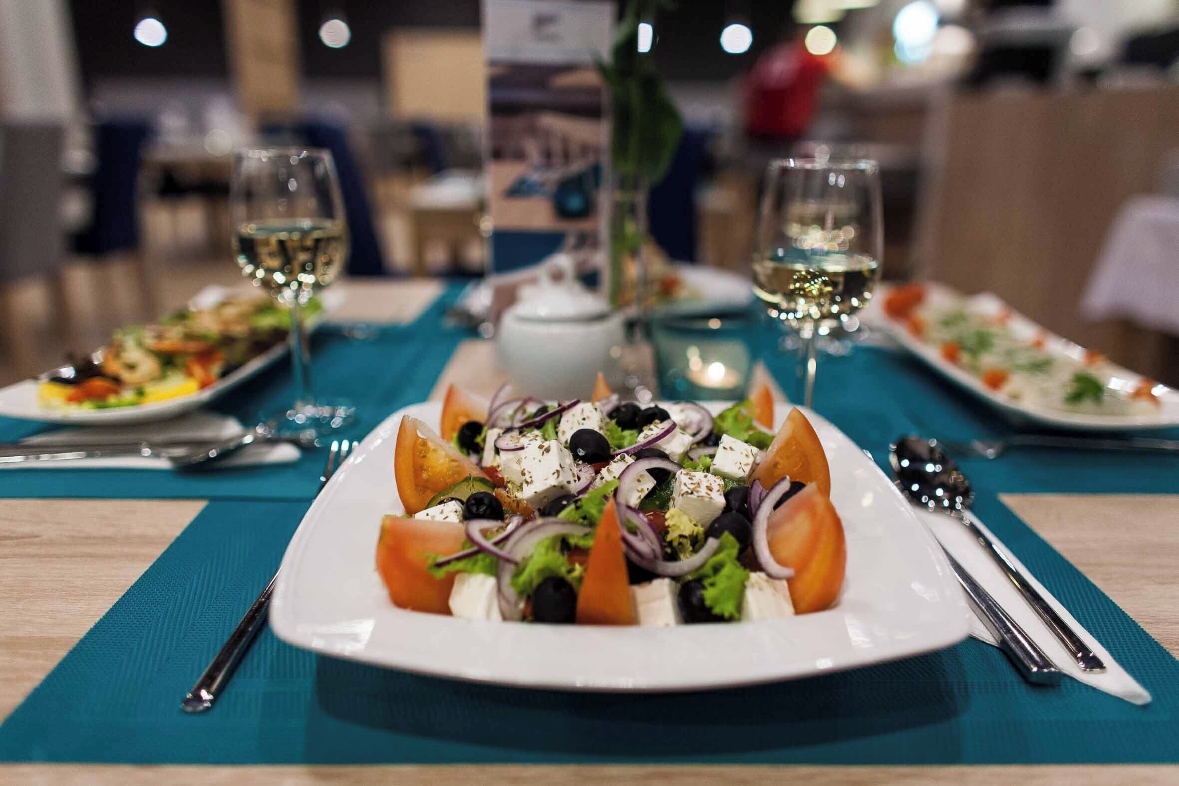 A dining table with a plate of salad, two glasses of white wine, and a vase of flowers.