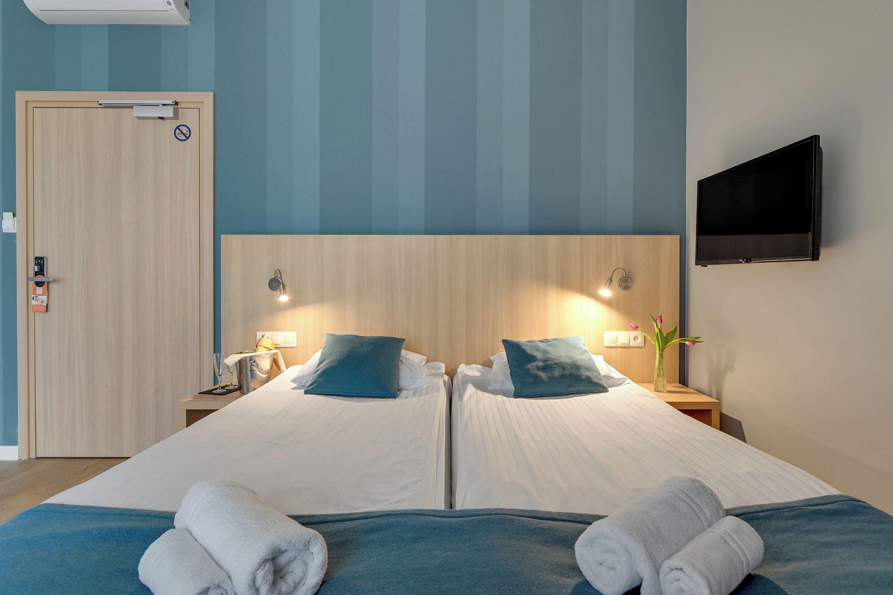 Habitació d'hotel amb dos llits, un televisor fixat a la paret i una porta amb un senyal de prohibit l'entrada.