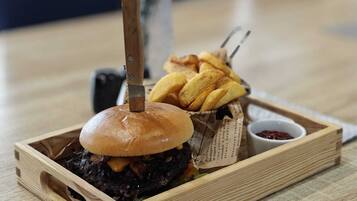 Una bandeja de madera con una hamburguesa, papas fritas y un vasito de salsa sobre una mesa.