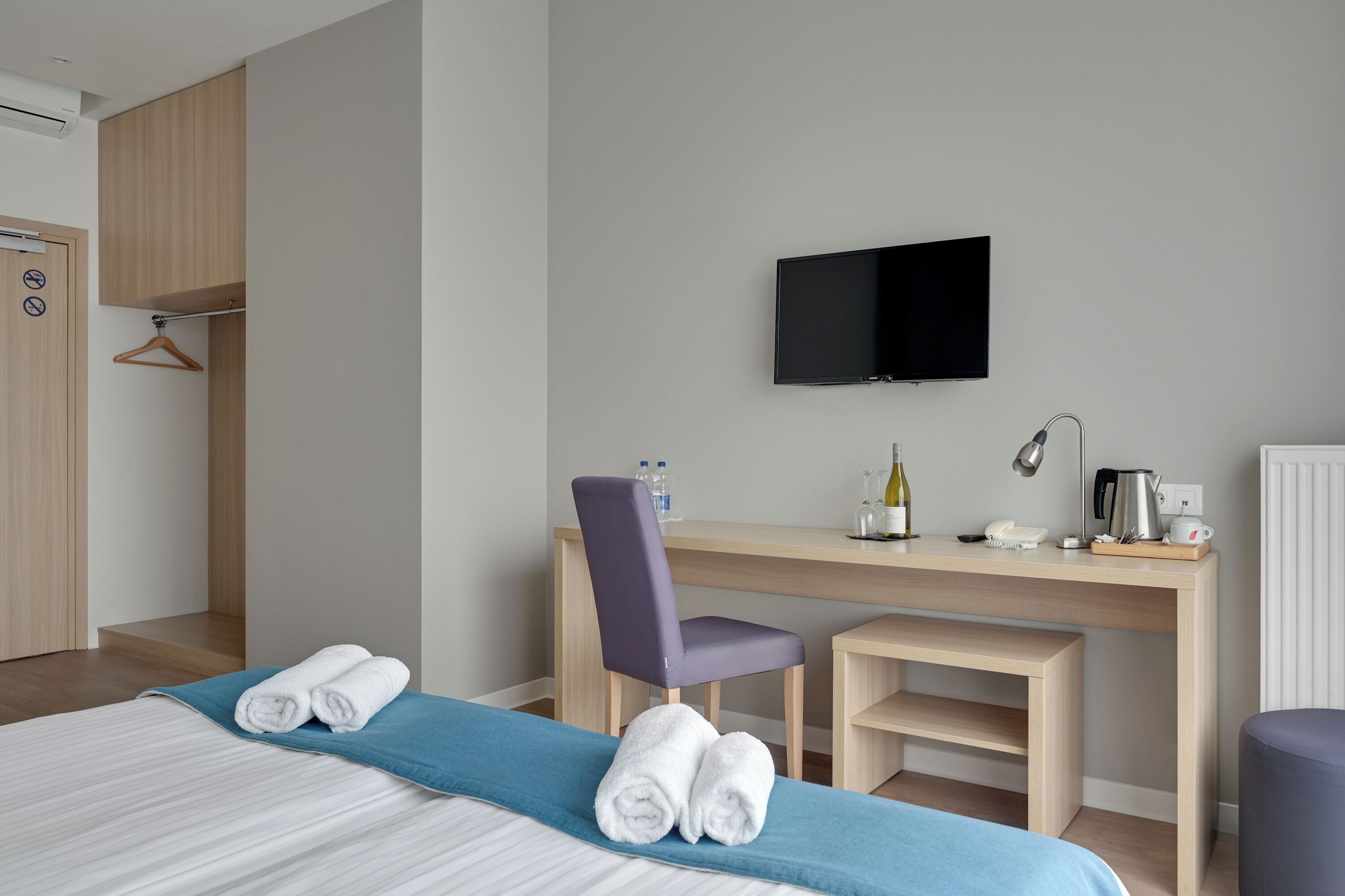 A hotel room with a bed, a desk with a chair, a television, and a wardrobe.