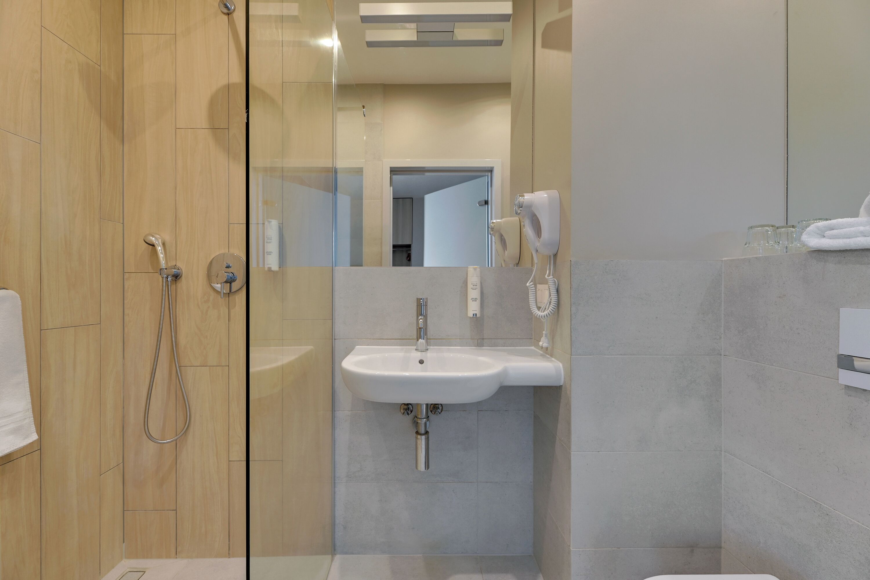 Un bagno moderno con doccia vetrata, lavandino bianco e soffione a mano.