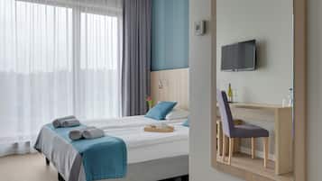 A hotel room with a bed, a desk, a chair, a TV, and a window with curtains.