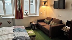Une pièce comprenant un lit, un canapé, un bureau avec une machine à écrire, une lampe et un téléviseur fixé au mur.