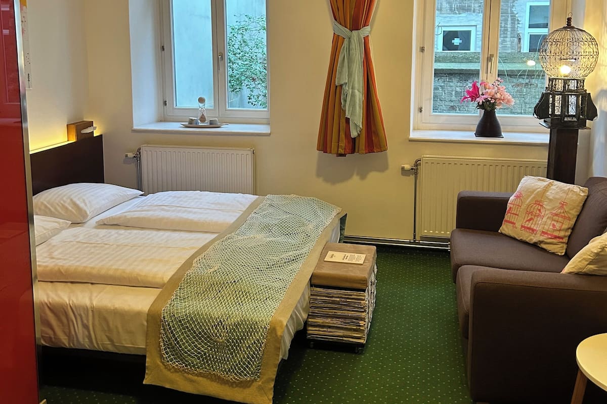 Una habitación de hotel con cama, sofá, una mesita y una ventana con cortinas.