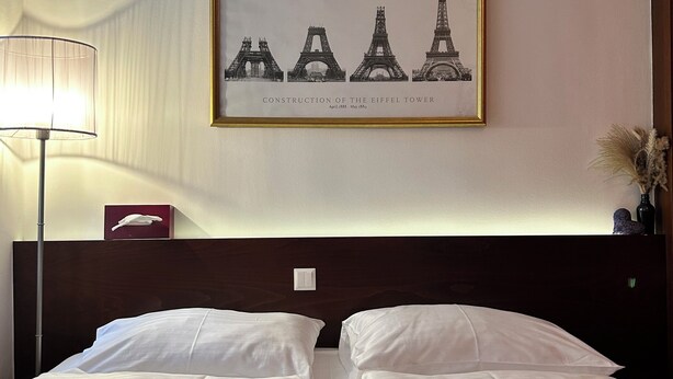 Une chambre d’hôtel avec un lit, un tableau encadré représentant la Tour Eiffel, une lampe et un petit objet décoratif sur la table de chevet.