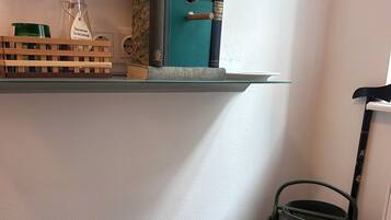 Una cocina con una mesa de madera, un hervidor verde, un comedero de pájaros y una estantería con libros y un recipiente de vidrio.