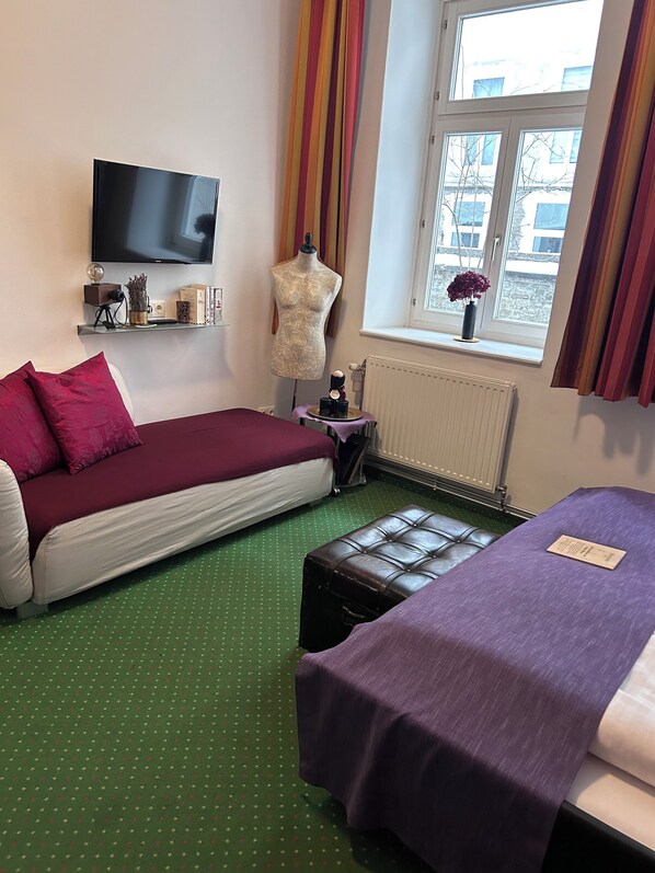 A hotel room with two beds, a television, a mannequin, and a window with curtains.