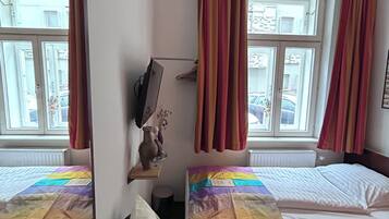 Une chambre avec deux lits, un miroir, une petite table avec un vase et une fenêtre avec des rideaux.