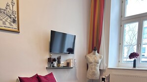 Une pièce comprenant un canapé-lit, un téléviseur, un mannequin et une fenêtre donnant sur des immeubles.
