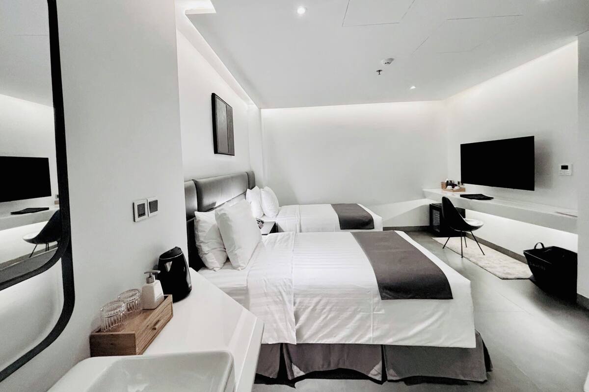 A modern hotel room with two beds, a flat-screen TV, a desk with a chair, and a large mirror.