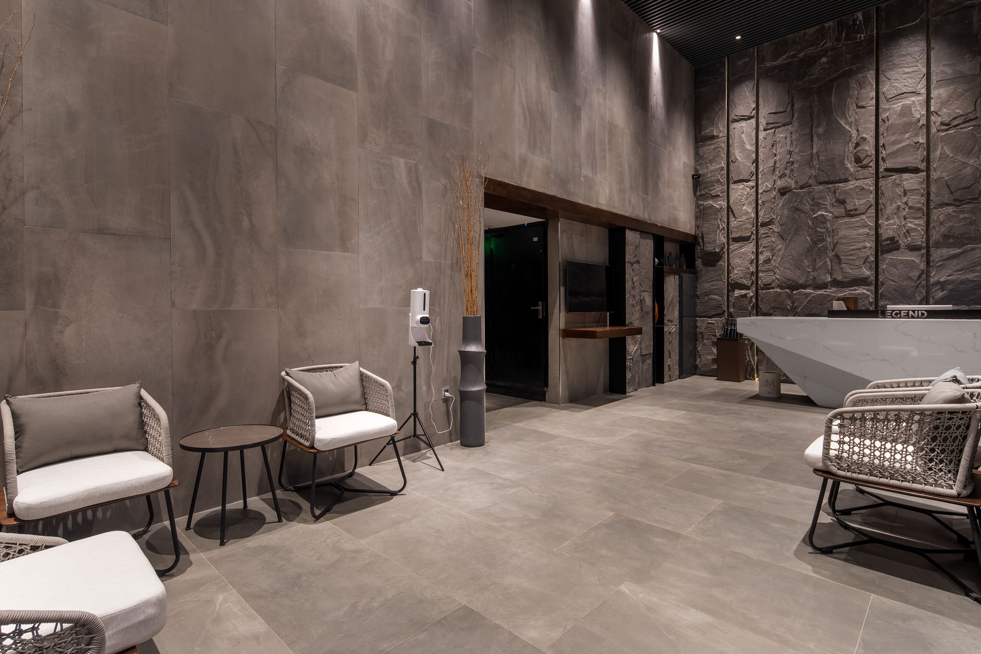 Un hall d’entrée moderne avec un mur en pierre, un comptoir d’accueil et des espaces de détente.