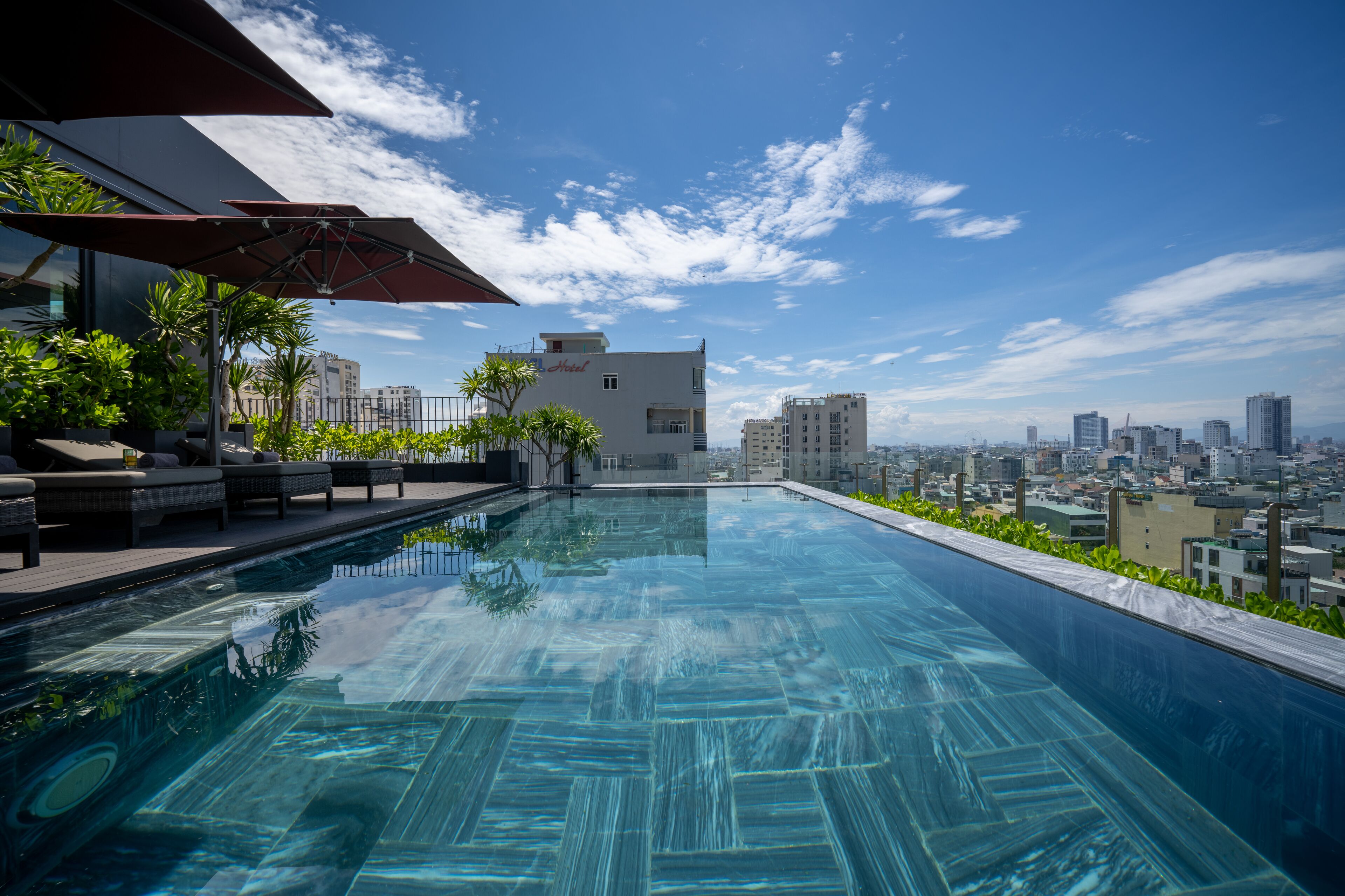 Ein Infinity-Pool auf dem Dach mit Blick auf die Stadt, Sitzgelegenheiten im Freien und einem Hotelgebäude im Hintergrund.