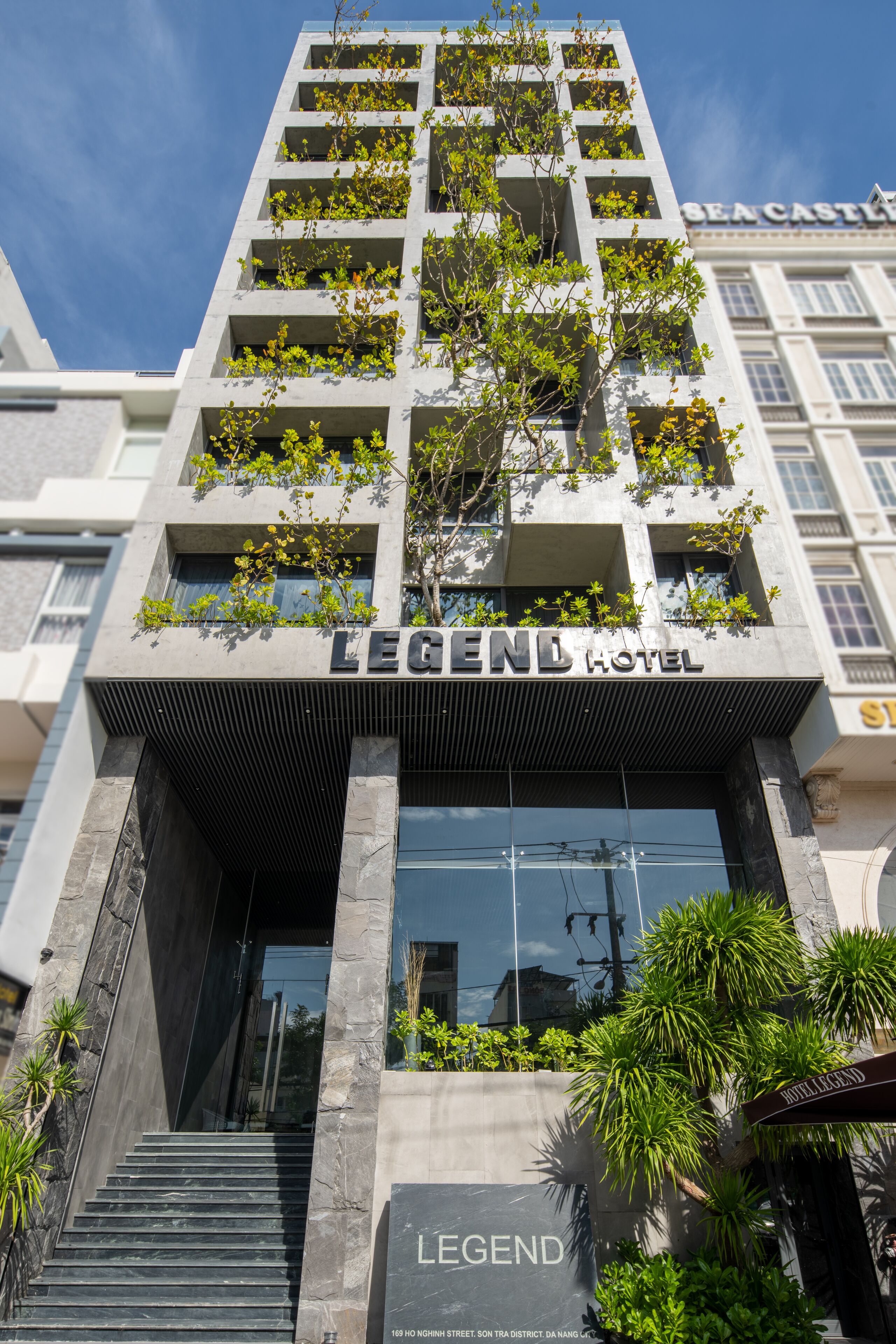 El exterior del Hotel Legend, con un diseño moderno, presenta una entrada destacada con escalones, un cartel y vistas de los edificios circundantes.
