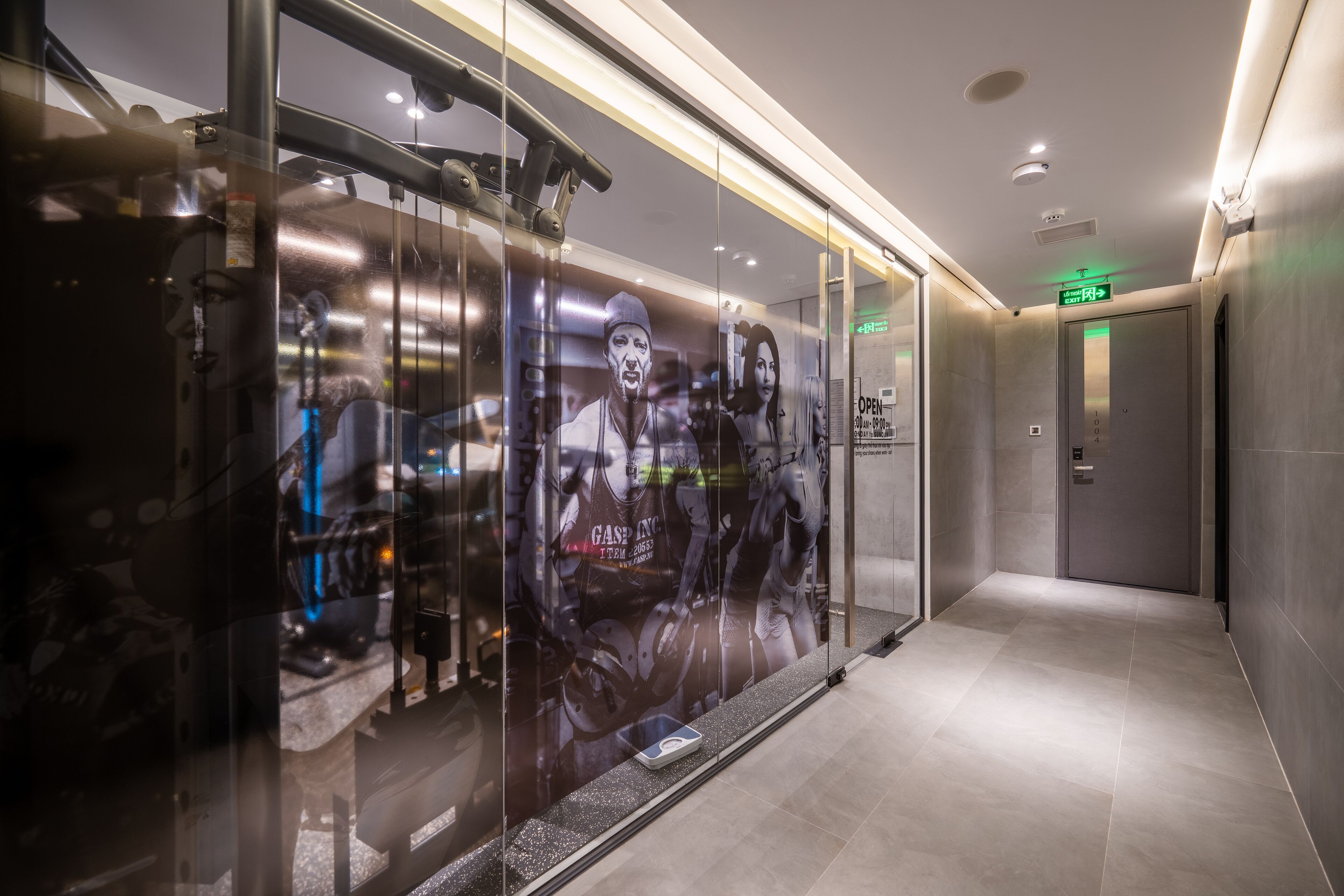 A modern elevator with a glass wall, a digital display, and a green exit sign.