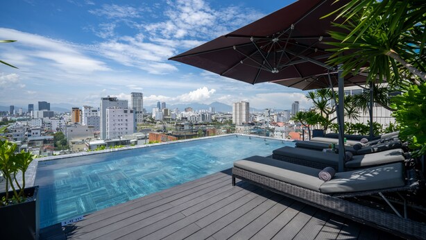 A rooftop infinity pool with a city view, lounge area with cushions, and a large umbrella. - LEGEND Boutique Hotel (Da Nang)