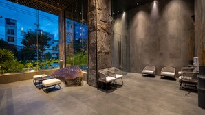 A modern indoor space with seating, a large stone pillar, and a view of the cityscape through large windows. - LEGEND Boutique Hotel (Da Nang)