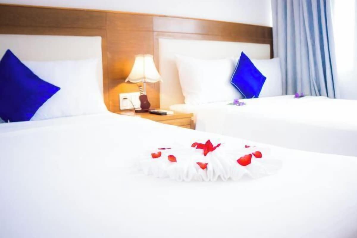 A hotel room with two beds, a nightstand with a lamp, and a decorative item on the bed.