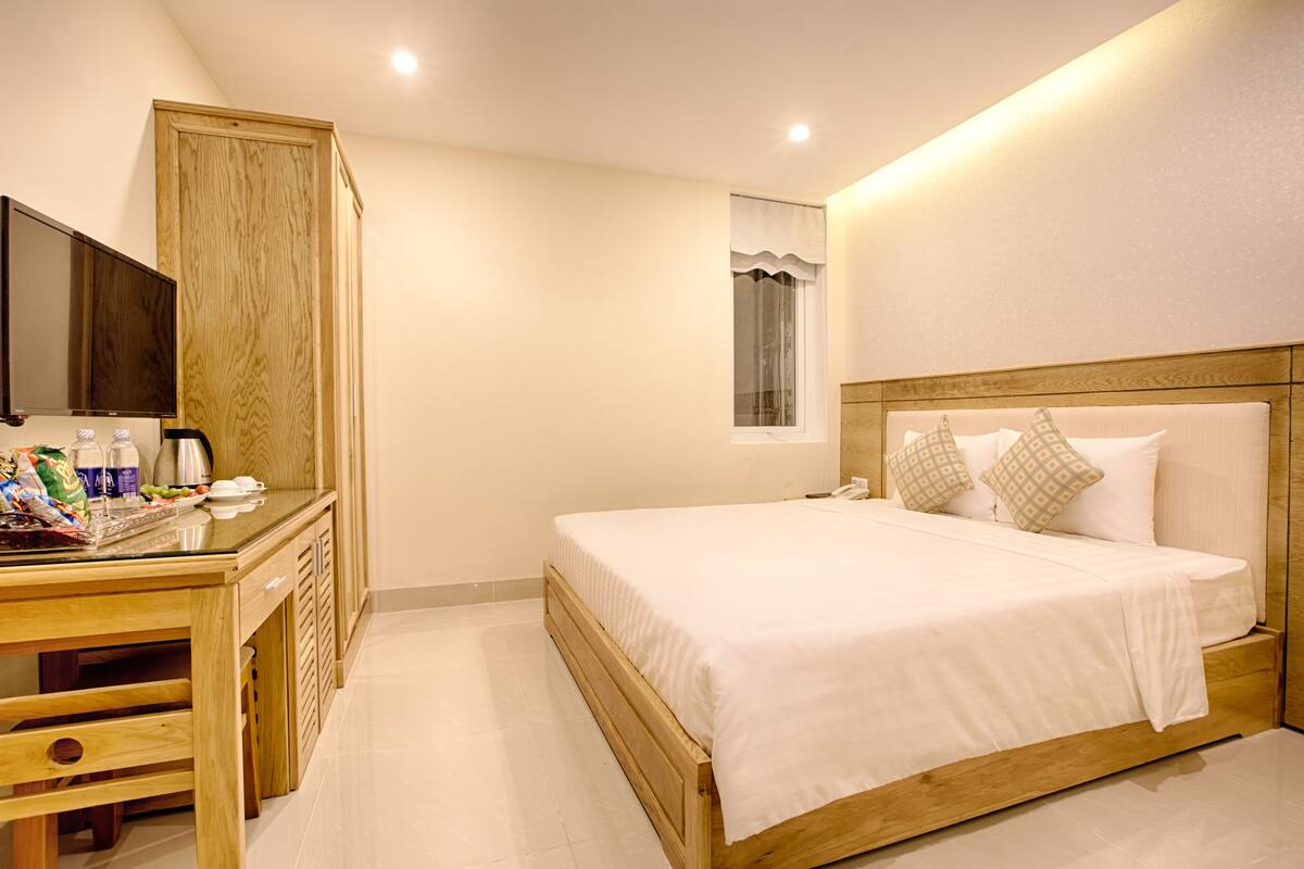 A hotel room with a wooden bed, a bedside table with a TV, and a window with curtains.
