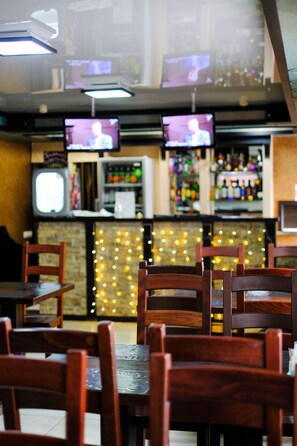 A bar area with multiple TVs, wooden chairs, and a bar counter with bottles.