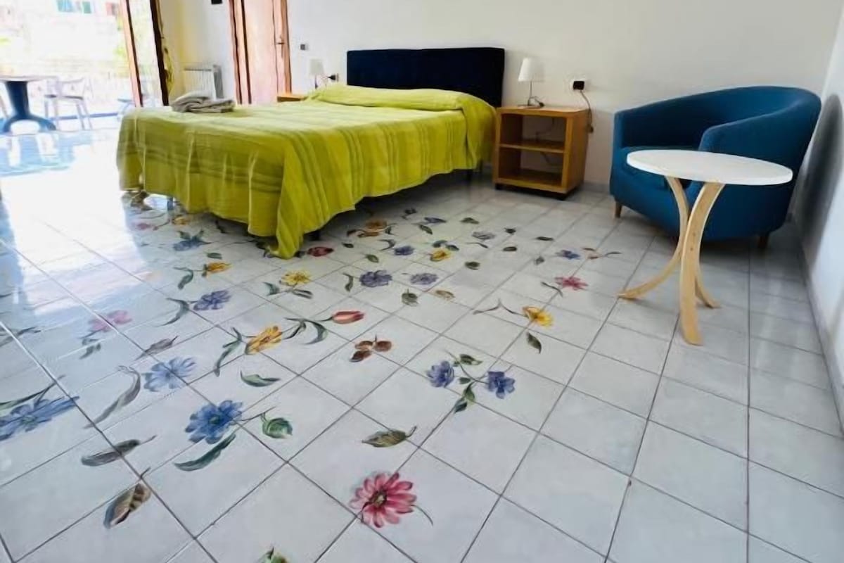 Una habitación con cama, una silla, una mesita y una puerta que da a un espacio exterior.