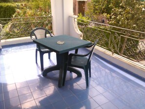 Un balcon agrémenté d’une table et de chaises, entouré d’une rambarde en métal et de verdure.