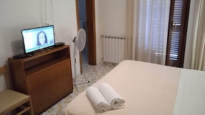 Une chambre d’hôtel avec un lit, un bureau avec un ordinateur, une chaise et un radiateur.