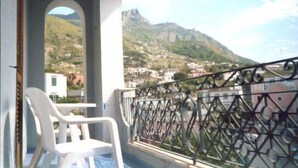 Un balcon avec des chaises en plastique blanches, une vue sur un paysage montagneux et une balustrade.