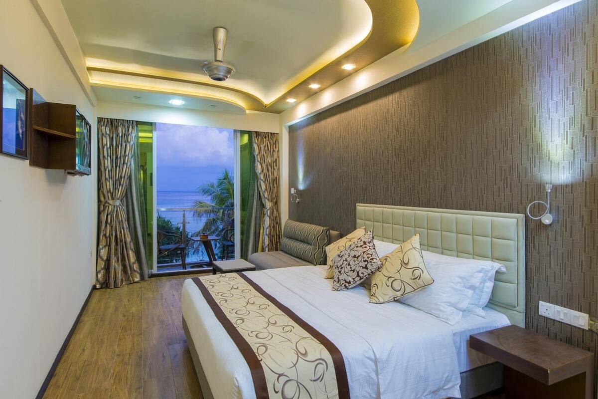 A hotel room with a large bed, a view of the ocean, and a balcony with a table and chairs.