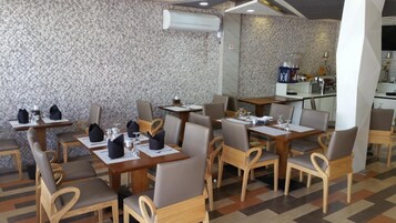 Un restaurante con mesas y sillas de madera, un muro de piedra y una zona de cocina al fondo.