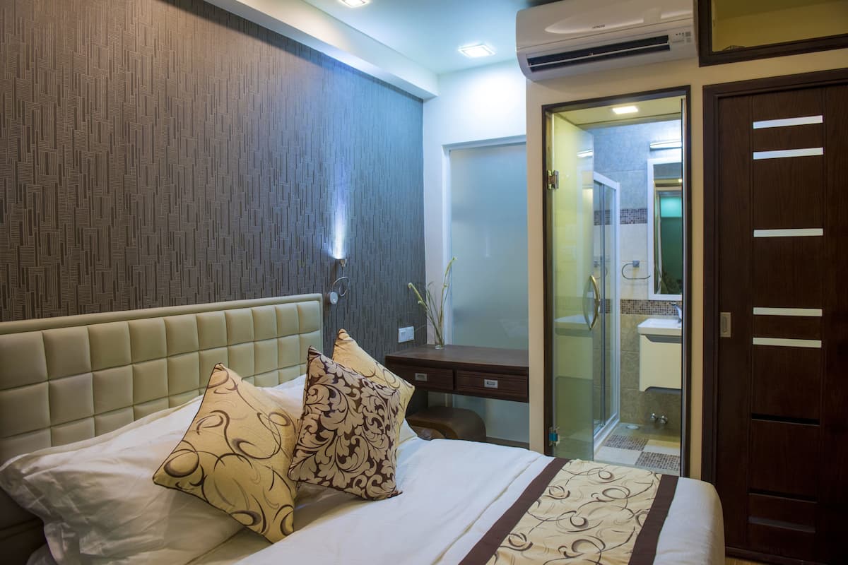 A hotel room with a bed, bedside table, and a bathroom visible through a glass door.