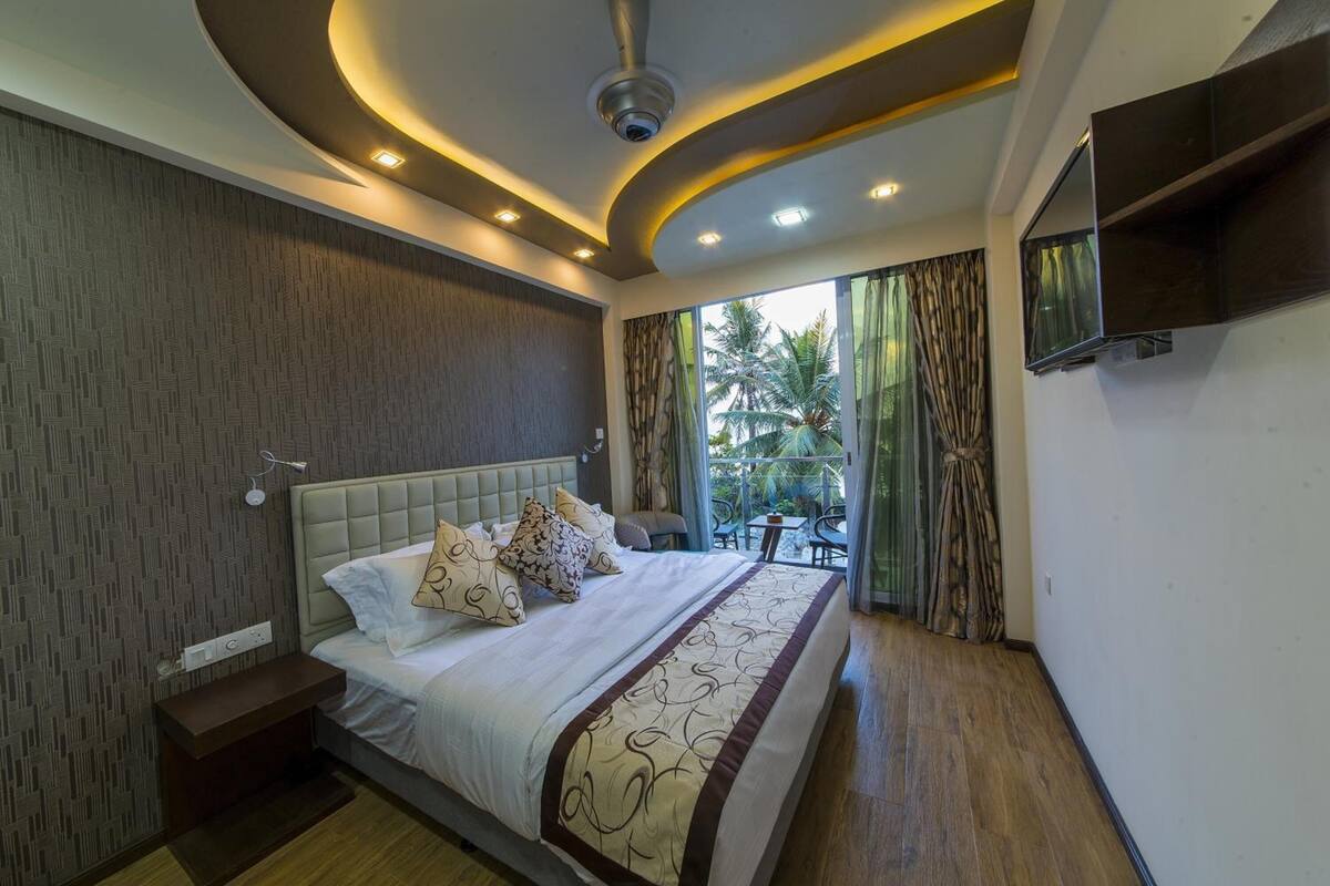 A modern bedroom with a large bed, a ceiling fan, recessed lighting, a TV, and a view of the outdoors.