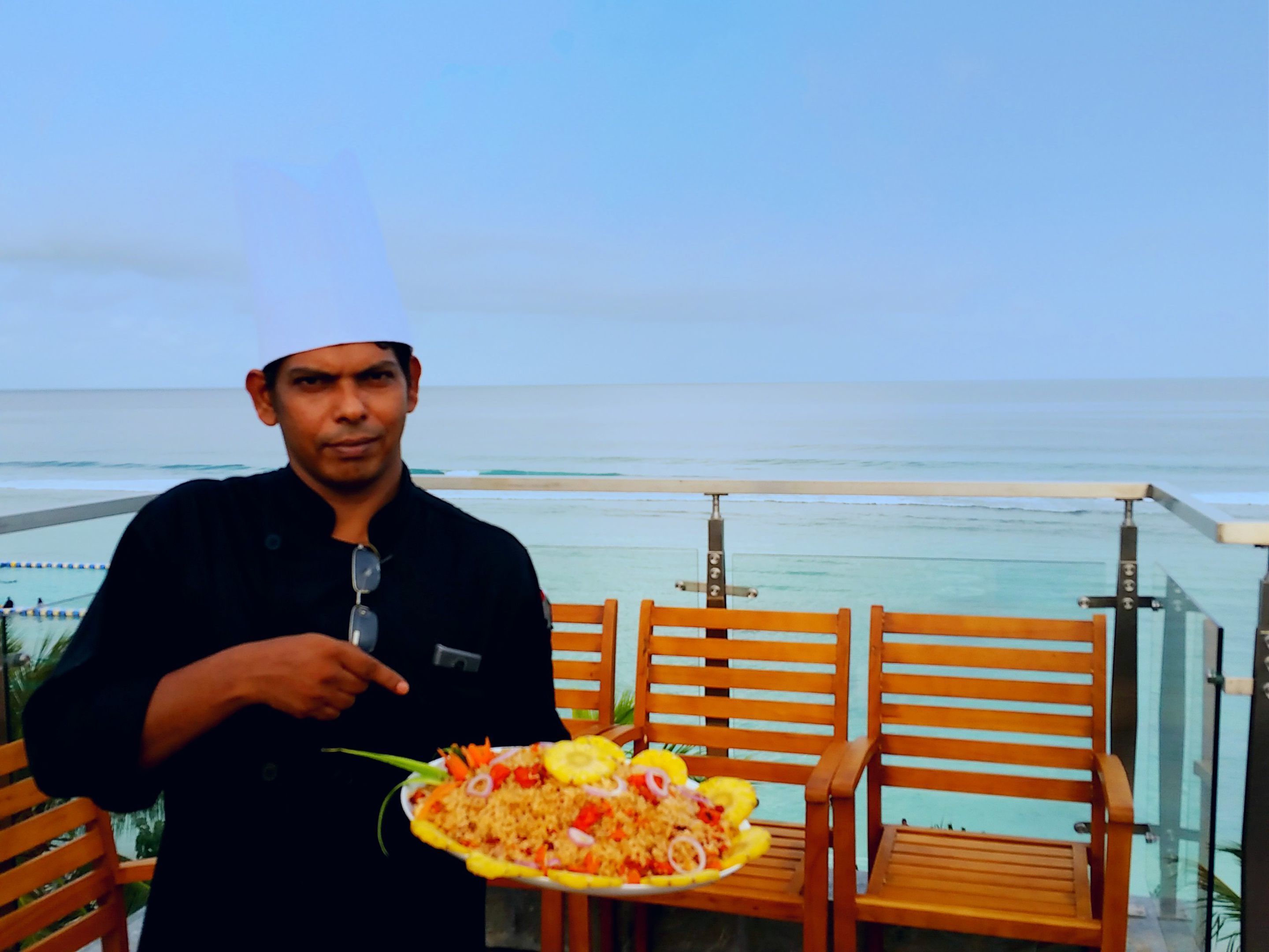 A person holding a plate of food with a view of the ocean in the background.