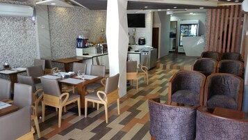 Un restaurante moderno con una mezcla de asientos de madera y tapizados, un suelo estampado y una zona de cocina al fondo.