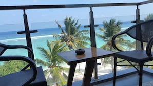 Un balcon avec vue sur l’océan et les palmiers, comprenant deux chaises et une petite table.