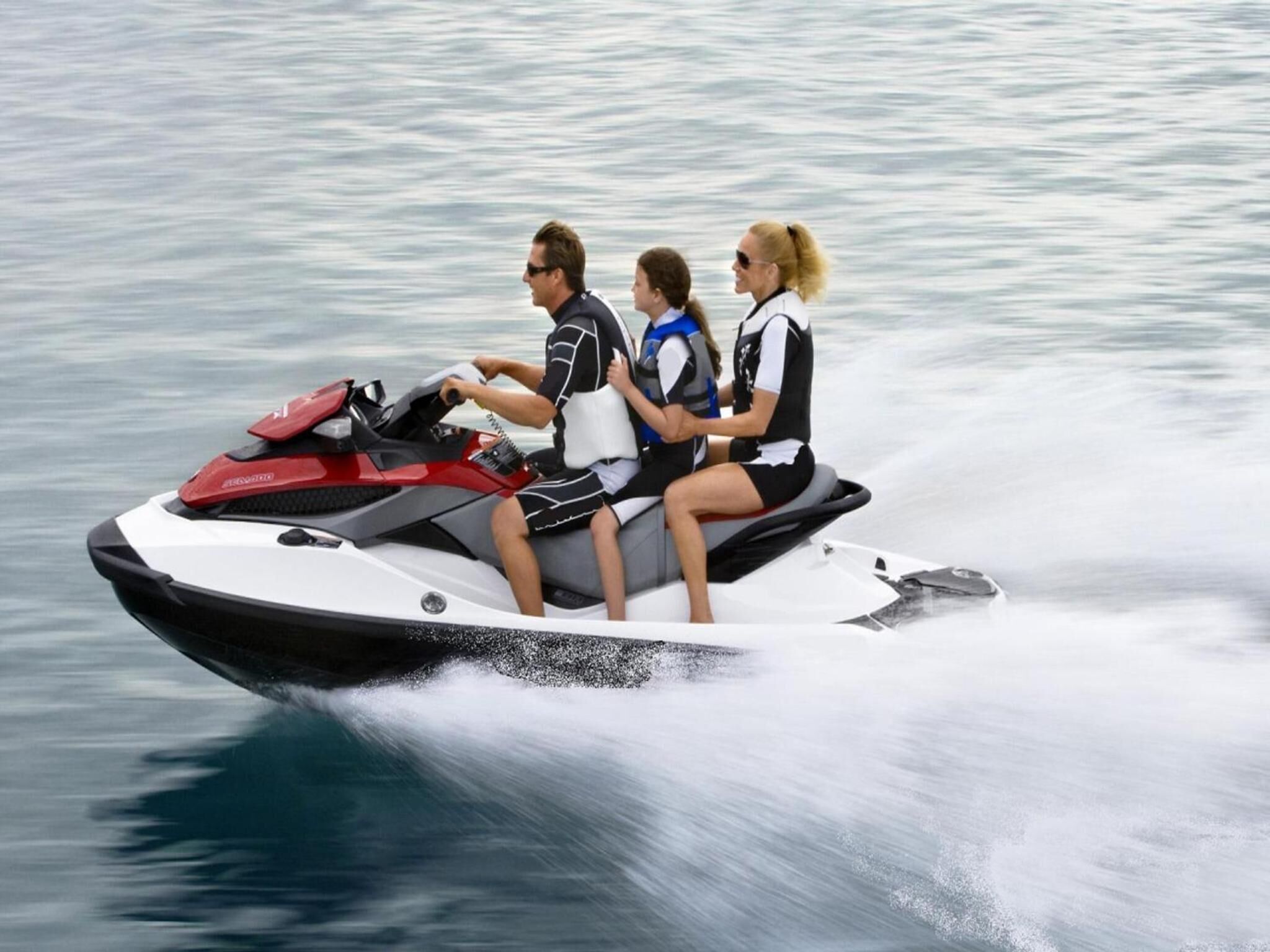Un jet ski con tres personas deslizándose sobre el agua.