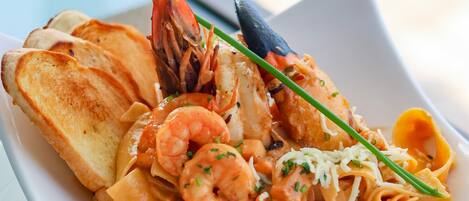 A seafood pasta dish with shrimp, mussels, and bread on a white plate.