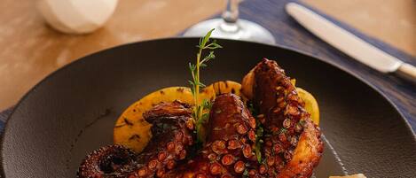 A plate of octopus with vegetables and a glass of white wine on a table.