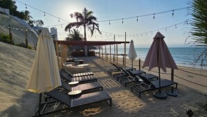 Un espace aménagé au bord de la plage, avec des chaises longues et des parasols, offrant une vue sur l’océan.