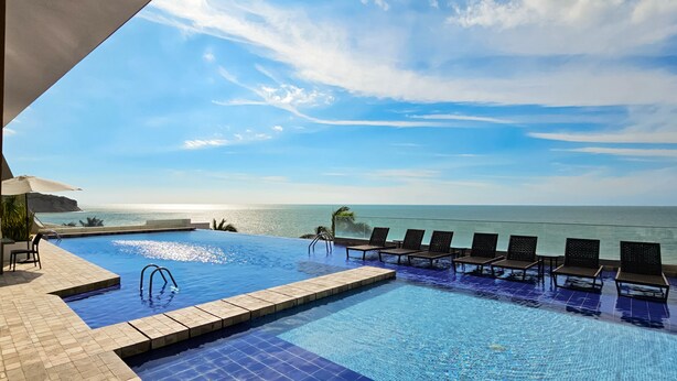 Une piscine avec vue sur l’océan, des chaises longues et un ciel dégagé.