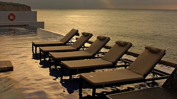 A poolside area with lounge chairs and a lifebuoy, overlooking the sea under a cloudy sky.