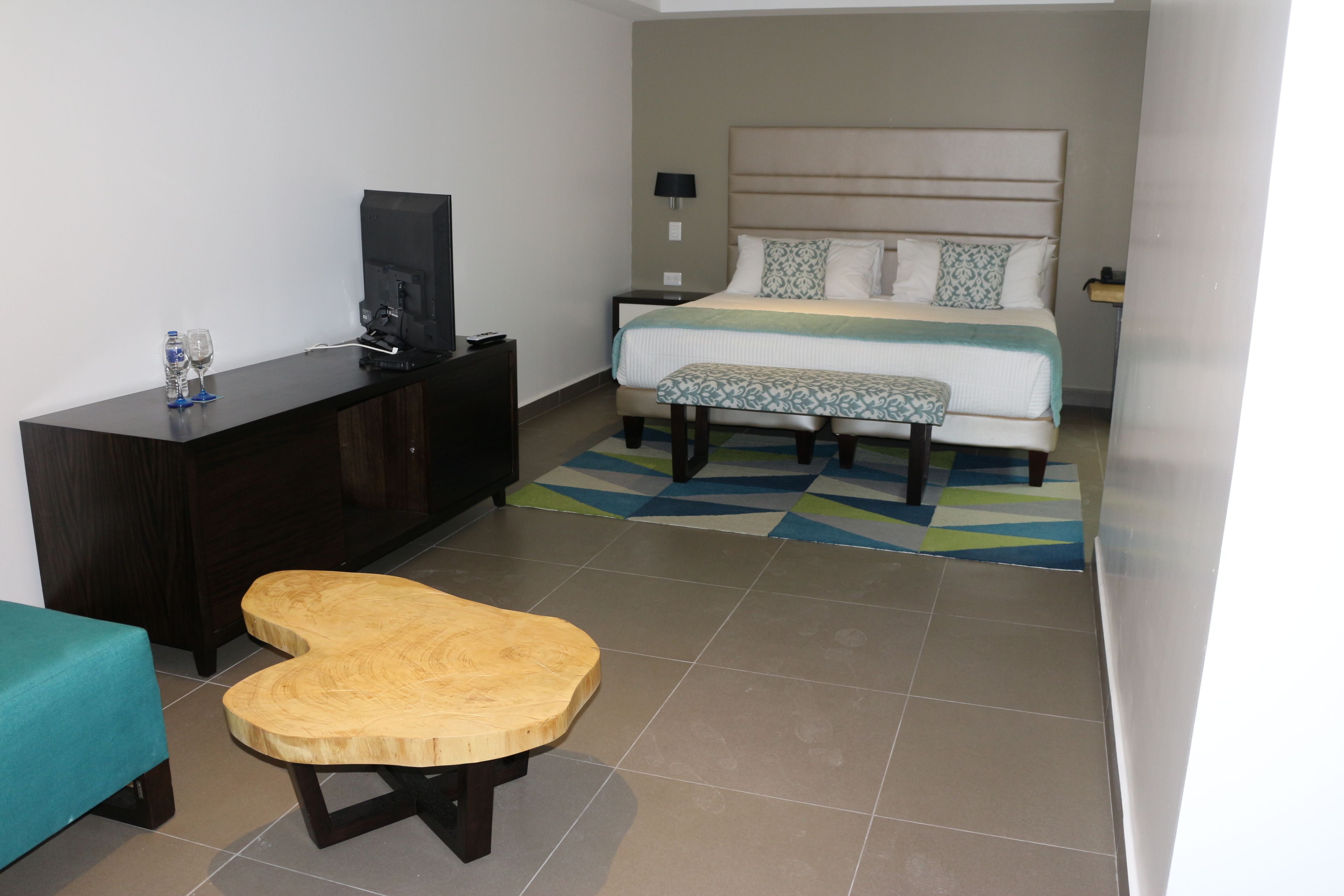 Une chambre d’hôtel avec un lit, une table de chevet, une télévision et un banc en bois.